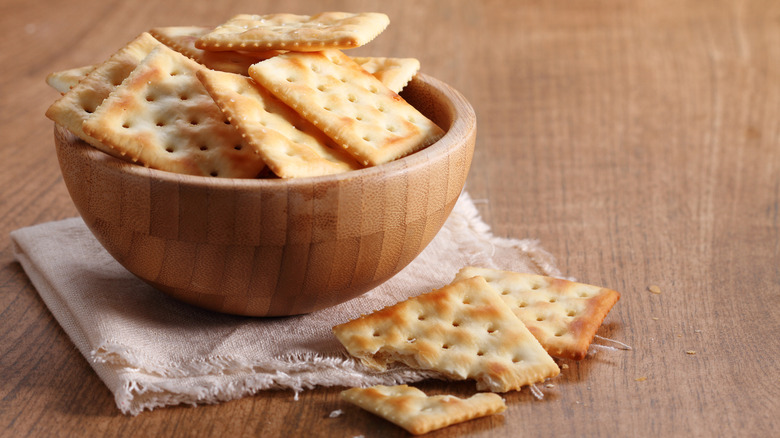 A close shot of a wooden bowl filled with crackers placed upon a cloth on a table