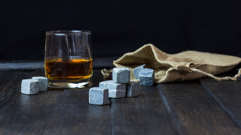 Several whiskey stones on a table with their bag and a filled glass of whiskey also shown