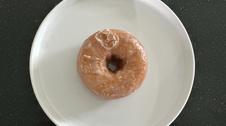 Overhead image of a glazed cake donut on white plate on black countertop