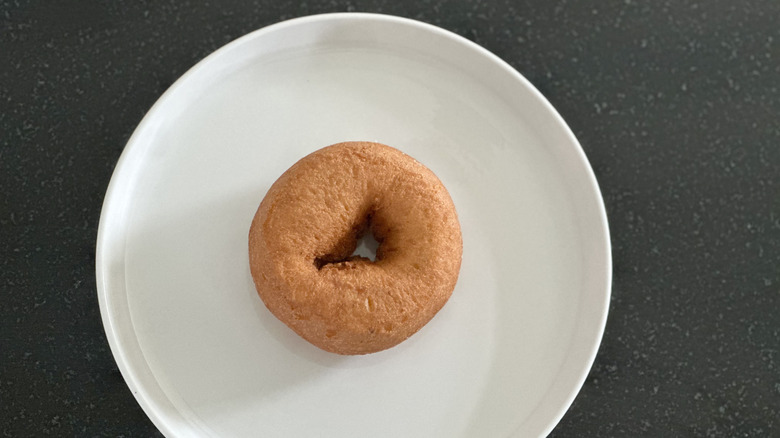 Overhead image of plain cake donut on white plate on black countertop