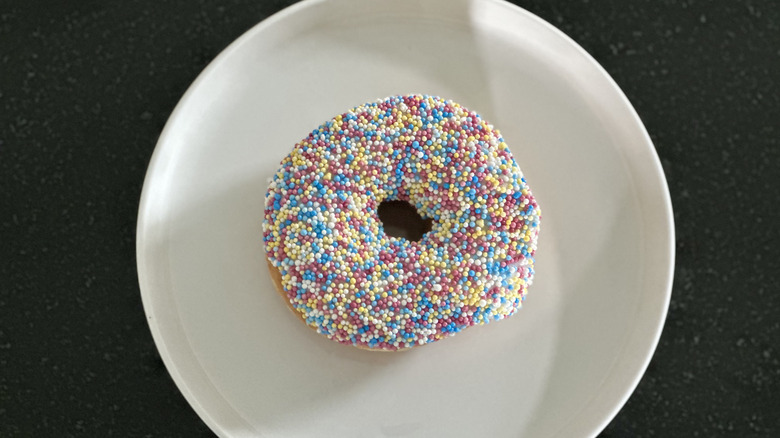 Overhead image of sprinkle donut on white plate on black countertop