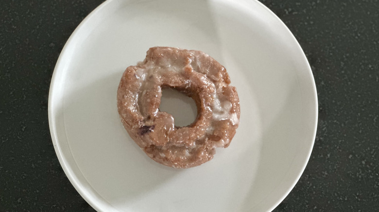 Overhead image of a glazed blueberry sour cream donut on white plate on black countertop
