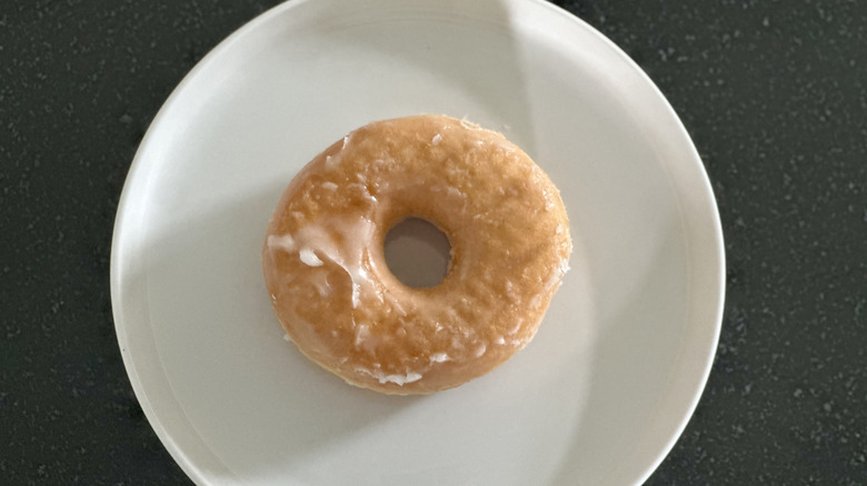 Overhead image of a glazed yeast donut on white plate on black countertop