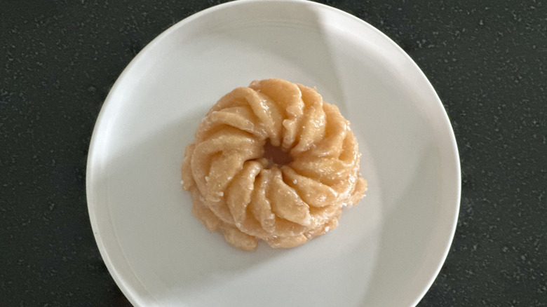 Overhead image of a honey cruller donut on white plate on black countertop