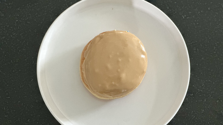 Overhead image of an iced maple donut on white plate on black countertop