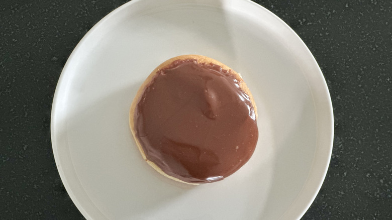 Overhead image of a chocolate iced Boston Cream donut on white plate on black countertop