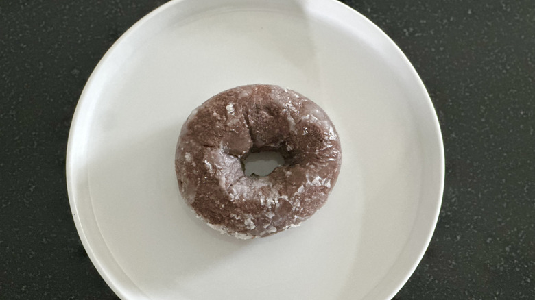 Overhead image of a glazed chocolate cake donut on white plate on black countertop