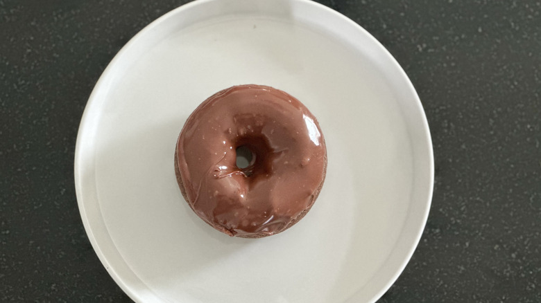 Overhead image of chocolate iced chocolate cake donut on white plate on black countertop