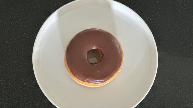 Overhead image of a chocolate iced donut on white plate on black countertop