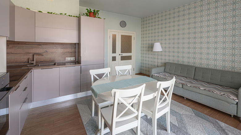 A very small kitchen with neutral dusty rose cabinets and light blue and gray color scheme in the other half of the room