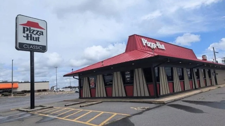 A pizza hut classic restaurant against cloudy sky with sign and parking lot outside