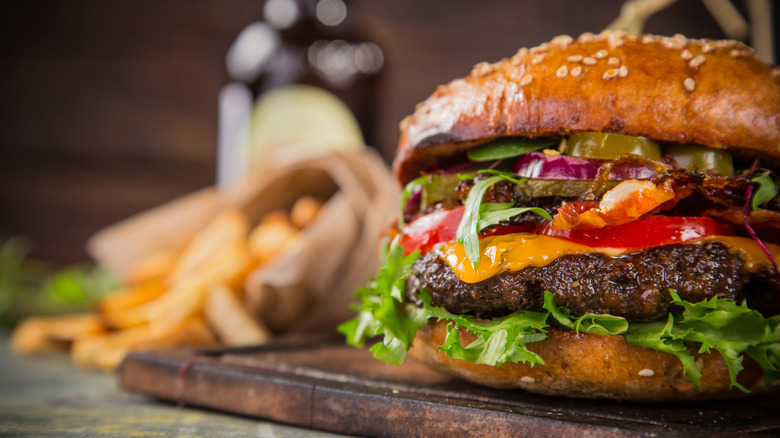 A close-up of a burger with toppings including cheese, lettuce, tomato, pickle, and onion