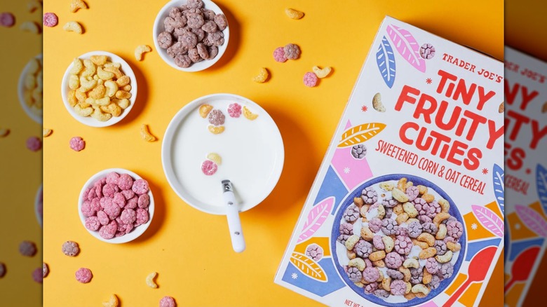 A box of Trader Joe's Tiny Fruity Cuties Cereal next to the cereal in bowls, one with milk, on an orange background