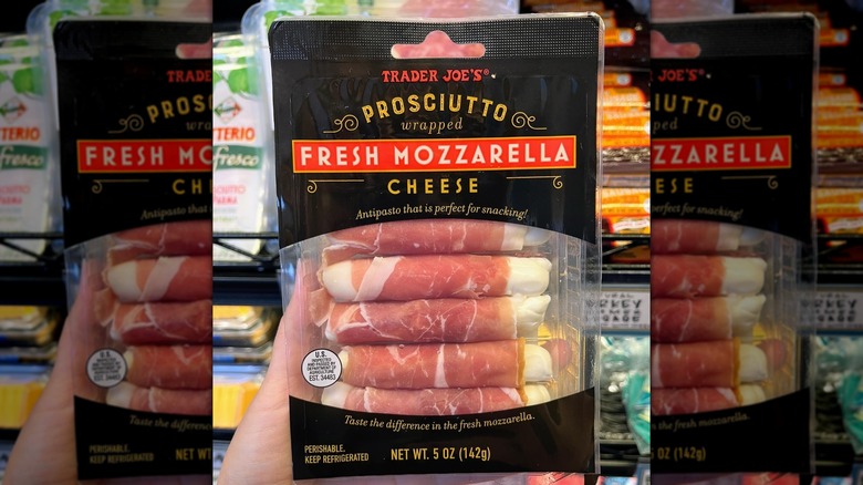 Hand holding package of Trader Joe's Prosciutto Wrapped Fresh Mozzarella Cheese in front of store shelf