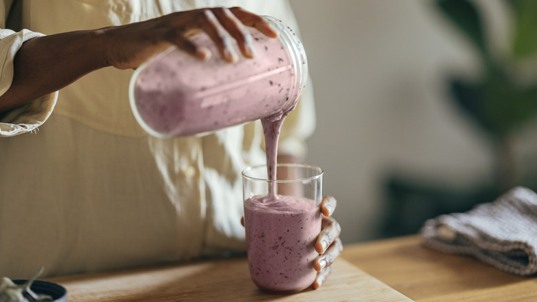 Hands pouring a berry smoothie out of a blender into a glass