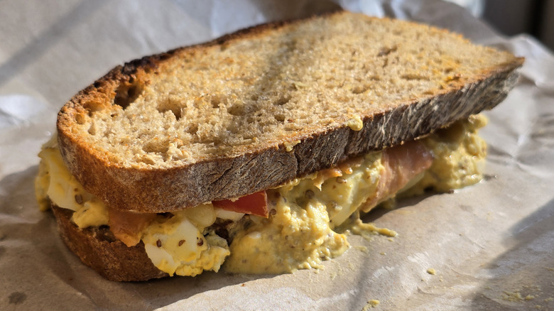 A close up of an egg salad sandwich on some brown paper
