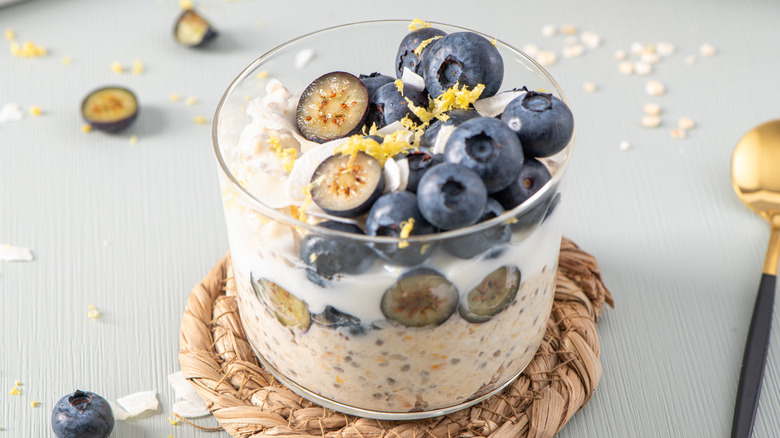 A glass jar of overnight oats topped with blueberries and lemon zest