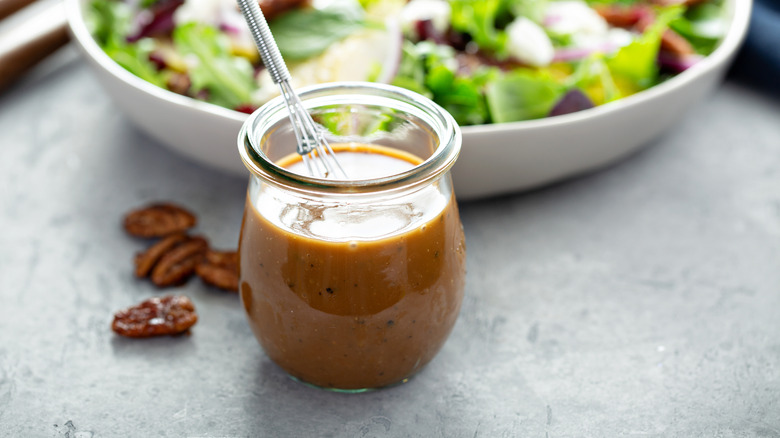 Homemade balsamic vinegar in a glass bowl with salad and nuts in the background