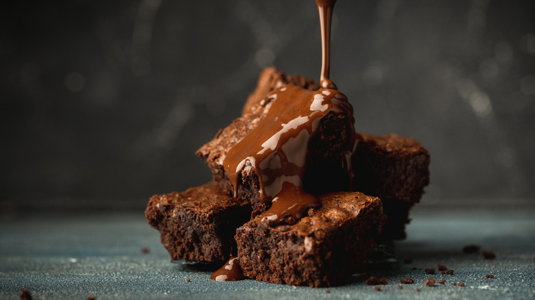 Drizzling dark melted chocolate over a pile of chocolate brownies