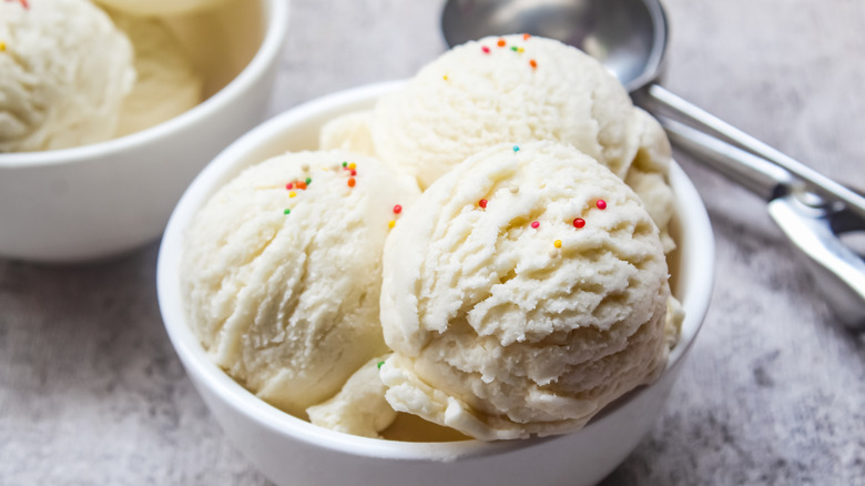Close up of three scoops of vanilla ice cream in a white bowl topped with colorful sprinkles