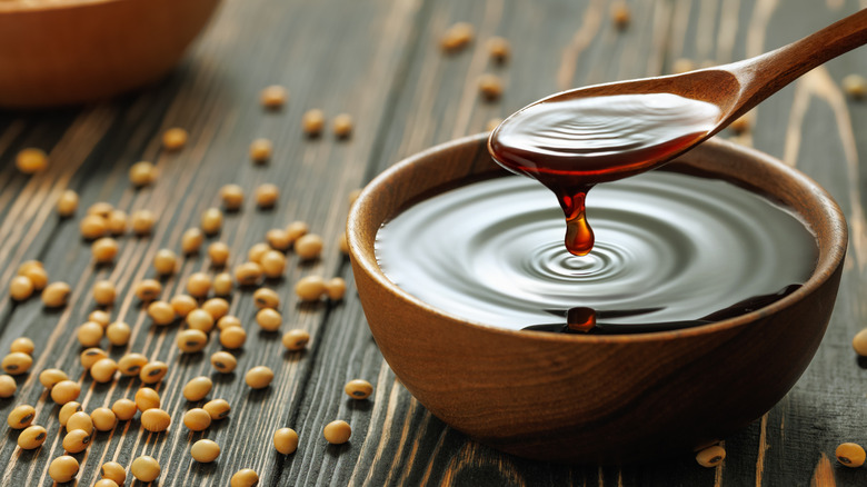 Spooning soy sauce in a small wooden dish surrounded by soy beans