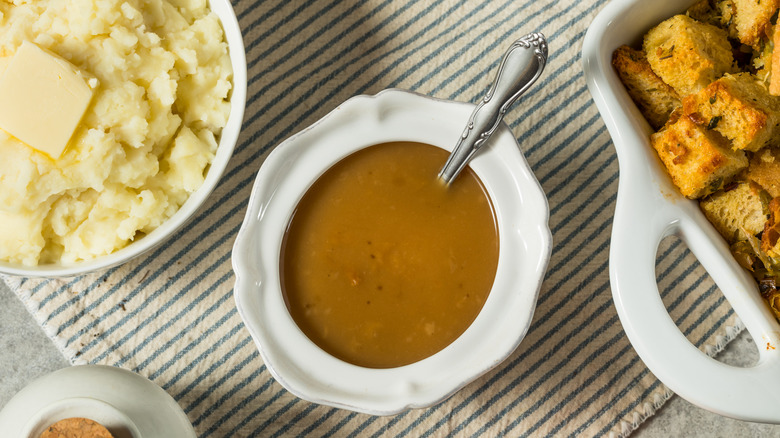 Homemade gravy in a dish surrounded with dishes filled with mashed potatoes and croutons