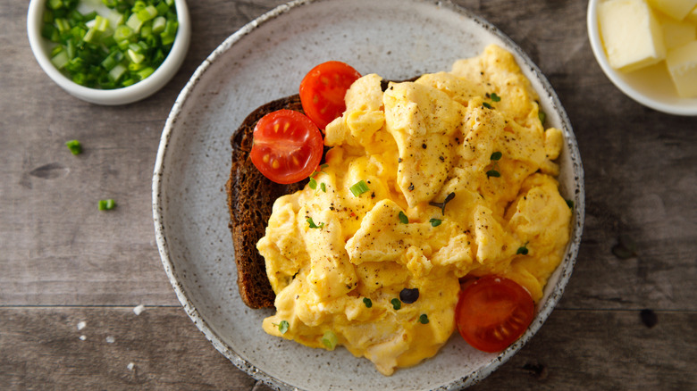 Traditional scrambled eggs over toast garnished with herbs and served with cherry tomatoes