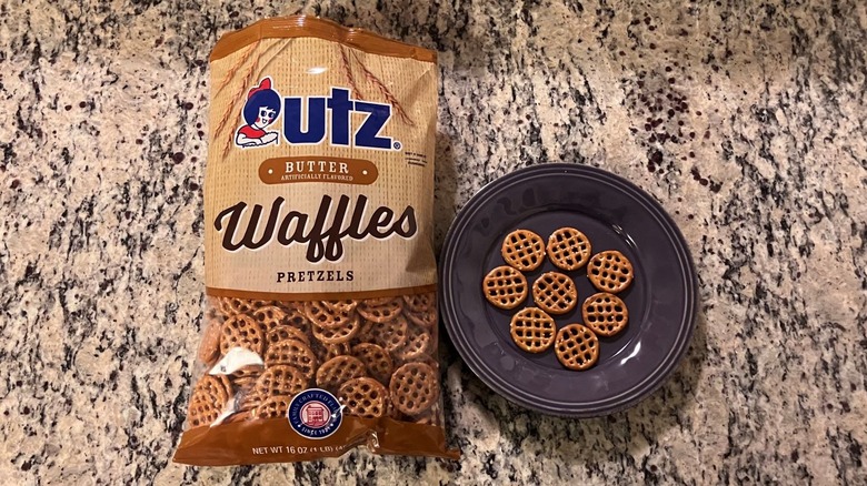 A bag of Utz Better Waffle Pretzels on a countertop next to a purple plate with eight pretzels on it