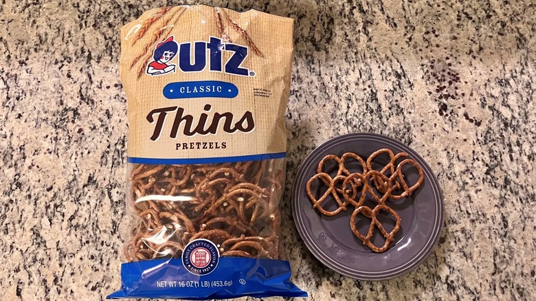 A bag of Utz Classic Thins Pretzels sits on a countertop next to a purple plate with six pretzels on it