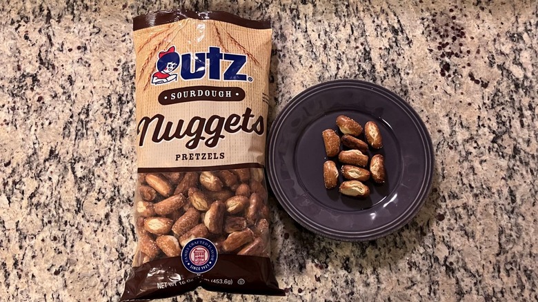 A bag of Utz Sourdough Nuggets Pretzels sits on a countertop next to a purple plate with nine pretzels on it