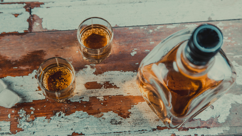 Old bottle of booze and two shots on paint chipped table