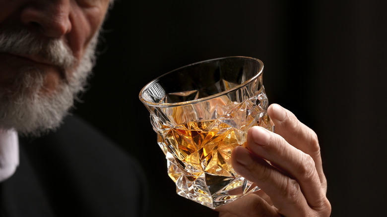A bearded person holding up a filled glass of whiskey
