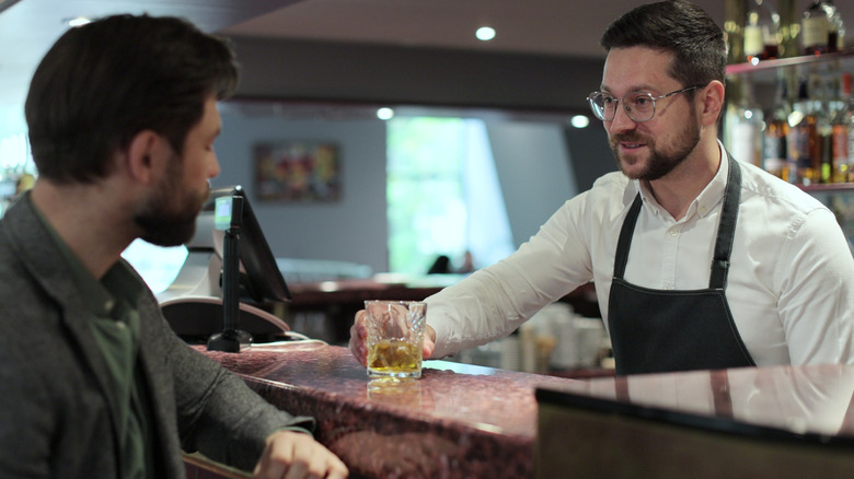 A bartender giving a glass of whiskey to to a customer
