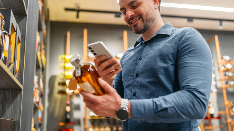 A person checking information on their phone while holding a liquor bottle
