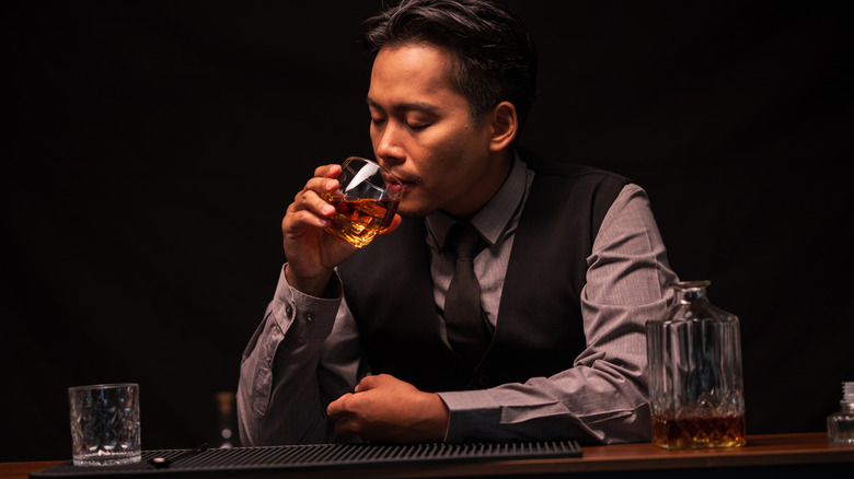 A person tasting whiskey at a bar with a darkened background