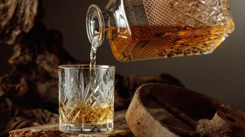 Whiskey being poured into a glass from an elaborate decanter in a rustic setting
