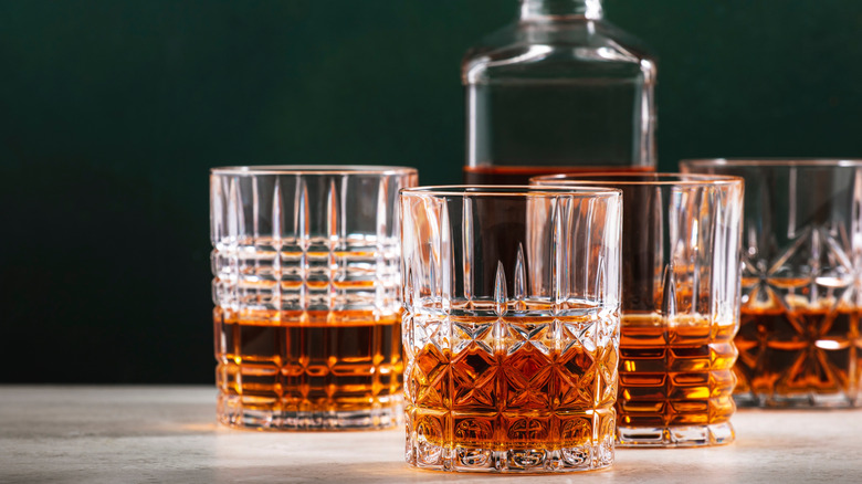 Four filled whiskey glasses shown with a unbranded bottle in the background