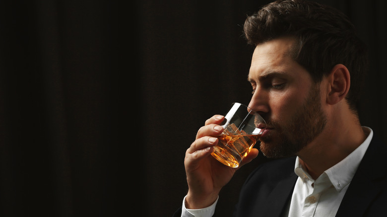 A person just about to taste whiskey from a tumbler with a dark background