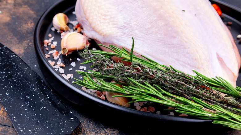 raw chicken breast shown on an black plate with garlic, coarse salt, rosemary, and thyme