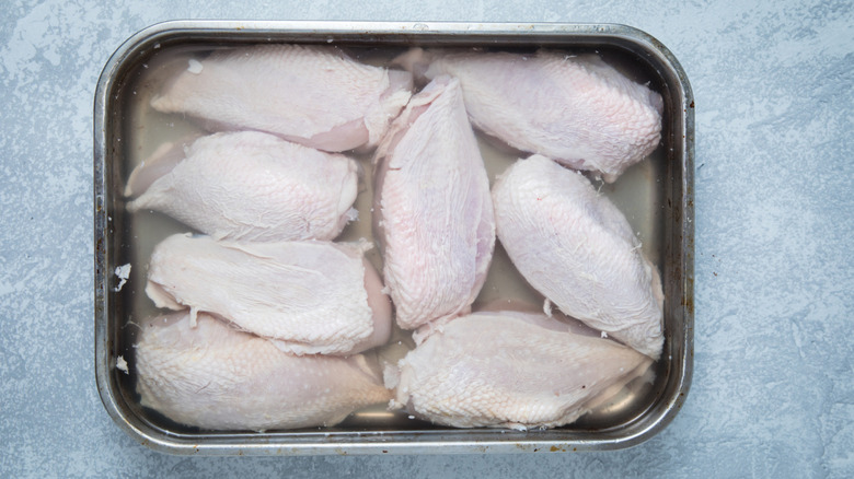 skin-on chicken breasts soaking in a steel pan of brine