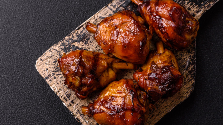 teriyaki-glazed chicken thighs, shown on a somewhat charred cutting board on a textured black countertop