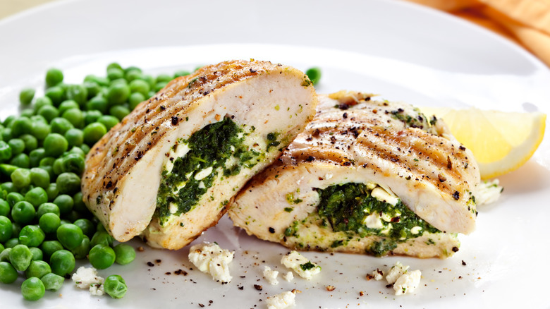 grilled chicken breast stuffed with spinach and cheese, cut in half for a more appealing presentation, served on a white plate with green peas and a lemon wedge