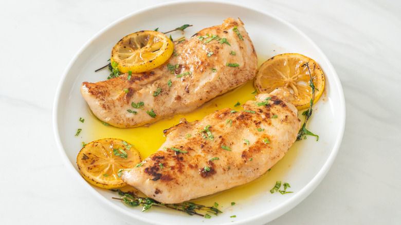 chicken breasts cooked with herbed butter and lemon, shown on a white plate with additional herbs and grilled lemon slices