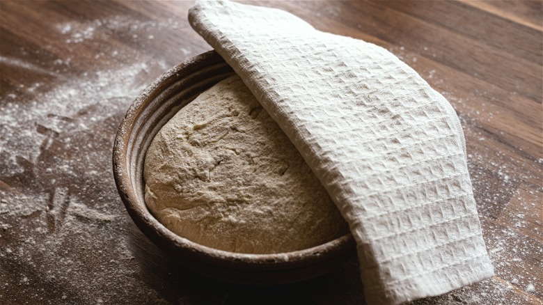 Dough proofing in bowl covered with towel on wooden table