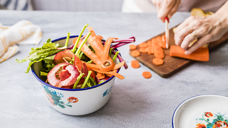 Food scraps in bowl next to person using a cutting board
