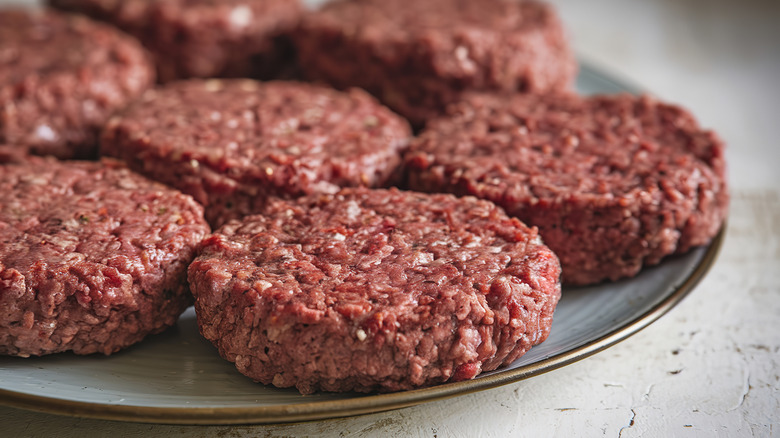 Raw burgers patties on plate