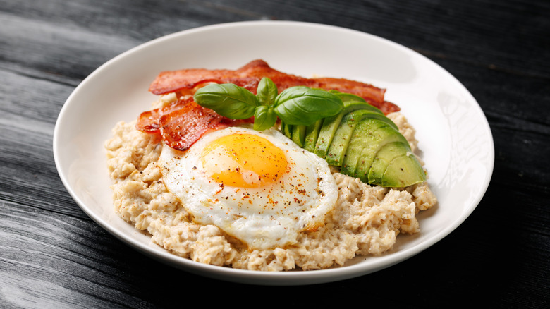 Bowl of savory oatmeal topped with fried egg, bacon and avocado
