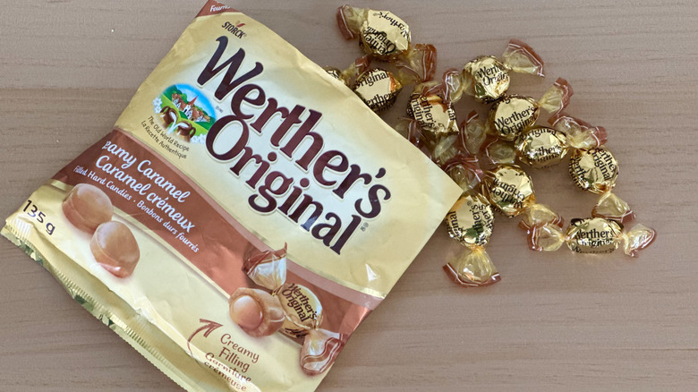 Open bag of Werther's Creamy Caramels with scattered wrapped candies on wooden table