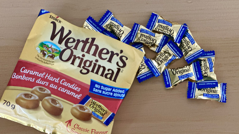 Open bag of Werther's No Sugar Added Hard Caramels with scattered wrapped candies on wooden table
