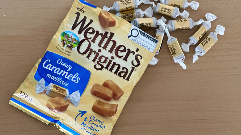 Open bag of Werther's Chewy Caramels with scattered wrapped candies on wooden table